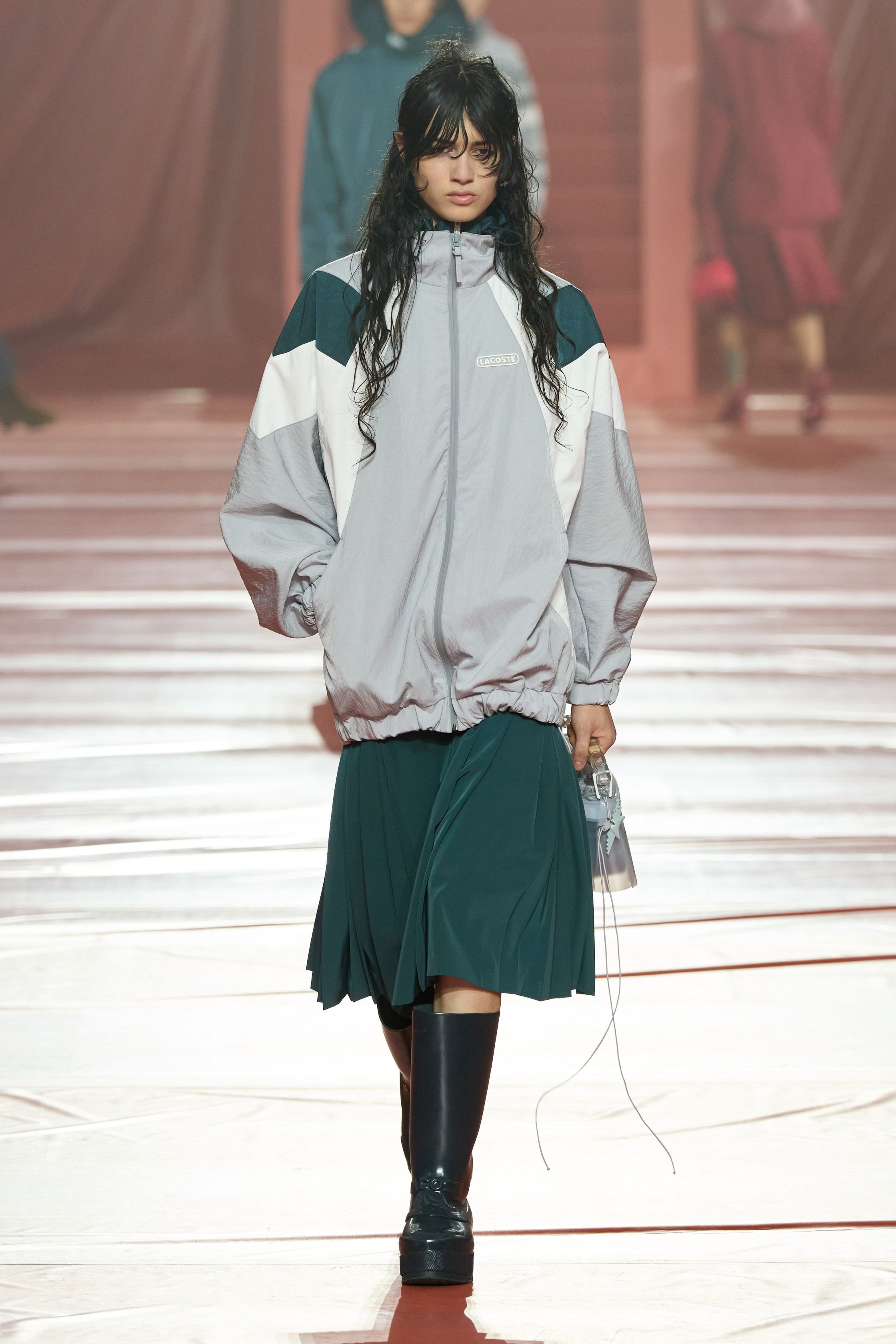 这一季 Lacoste 将品牌最核心的运动基因彻底升级为都市机能时装：酒红色尼龙运动外套、宽体运动裙、拉链高领和oversize运动风衣贯穿整场，经典网球白与深绿被重新调和成更成熟的学院运动色谱。轮廓保持宽松与机能感，但通过女性化中长裙、修身针织和高跟鞋完成优雅转换，使运动不再只是休闲，而是城市女性的日常盔甲-顽石频道趋势研究